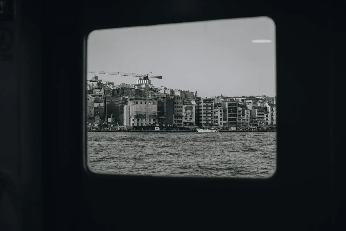 Monochrome view of a coastal city through a window frame, highlighting urban buildings and waterfront.