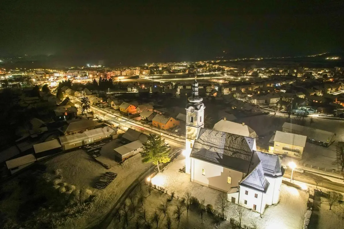 Aerial drone shot capturing a snow-covered town and illuminated church at night, showcasing winter scenery.