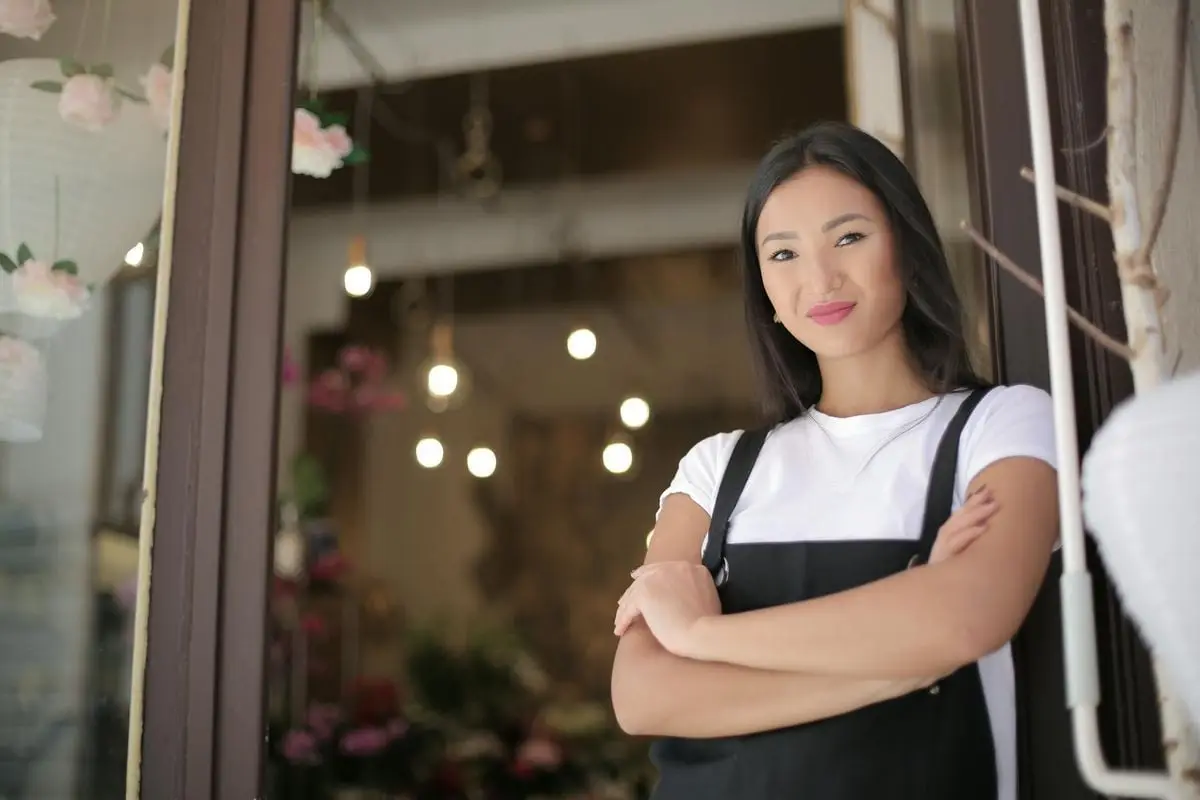 Smiling female florist standing with arms crossed at shop entrance, exuding confidence and friendliness.