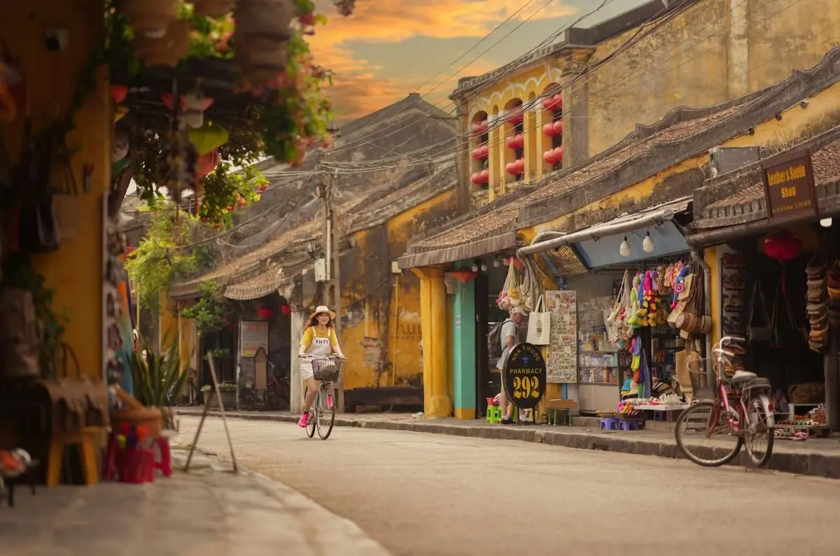 Woman cycling through a quaint street lined with shops in a traditional Asian village at dusk.