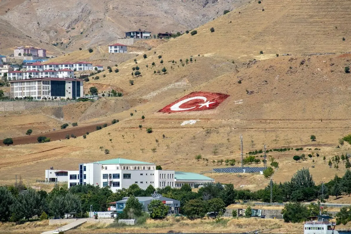 Pertek landscape featuring buildings and Turkish flag on arid hillside.