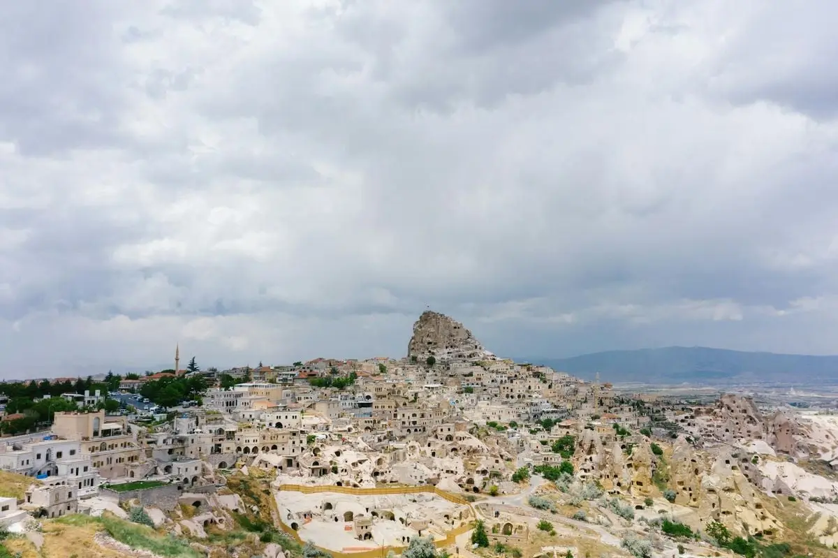 A scenic aerial view of the historic Uchisar Castle and town in Cappadocia, Turkey under overcast skies.