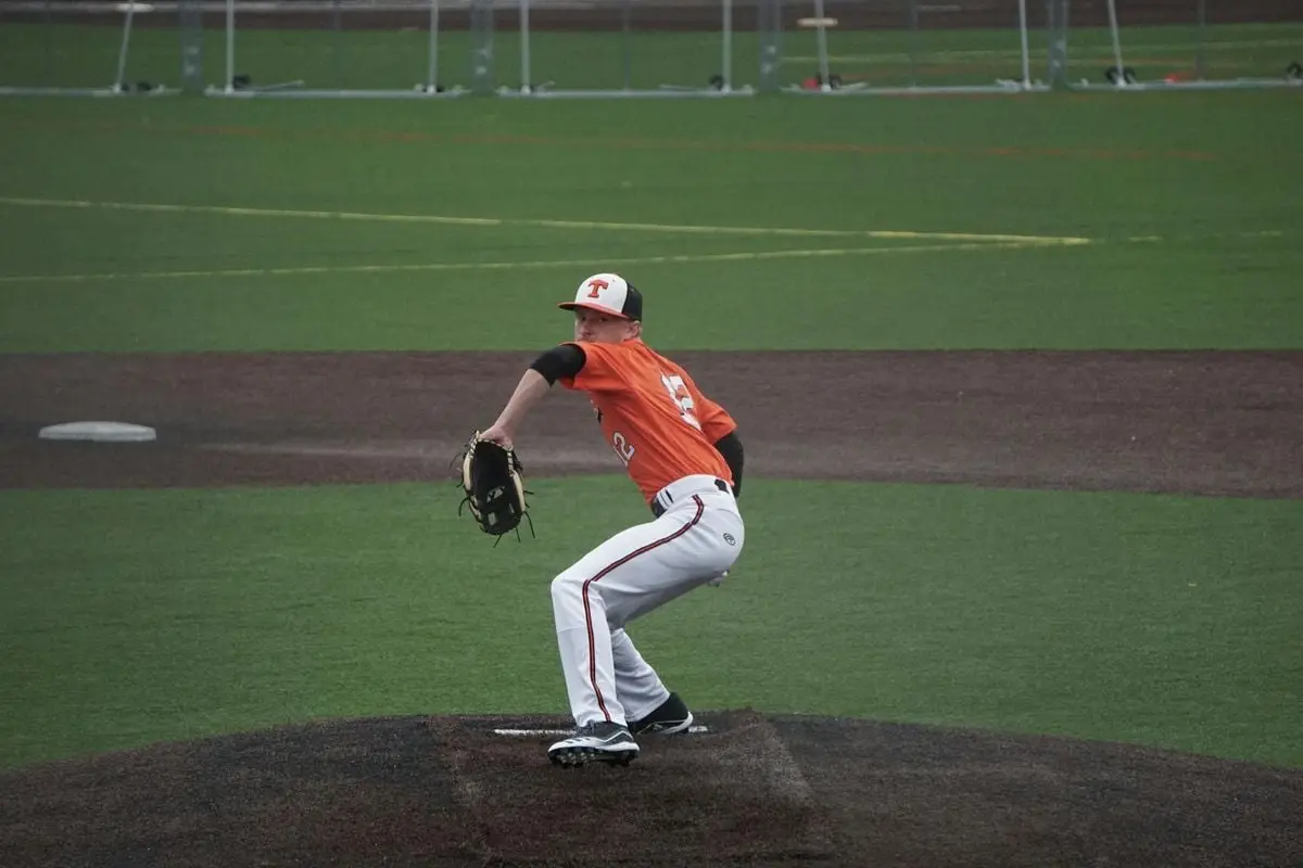 A baseball player in action, pitching on a sports field wearing an orange jersey.