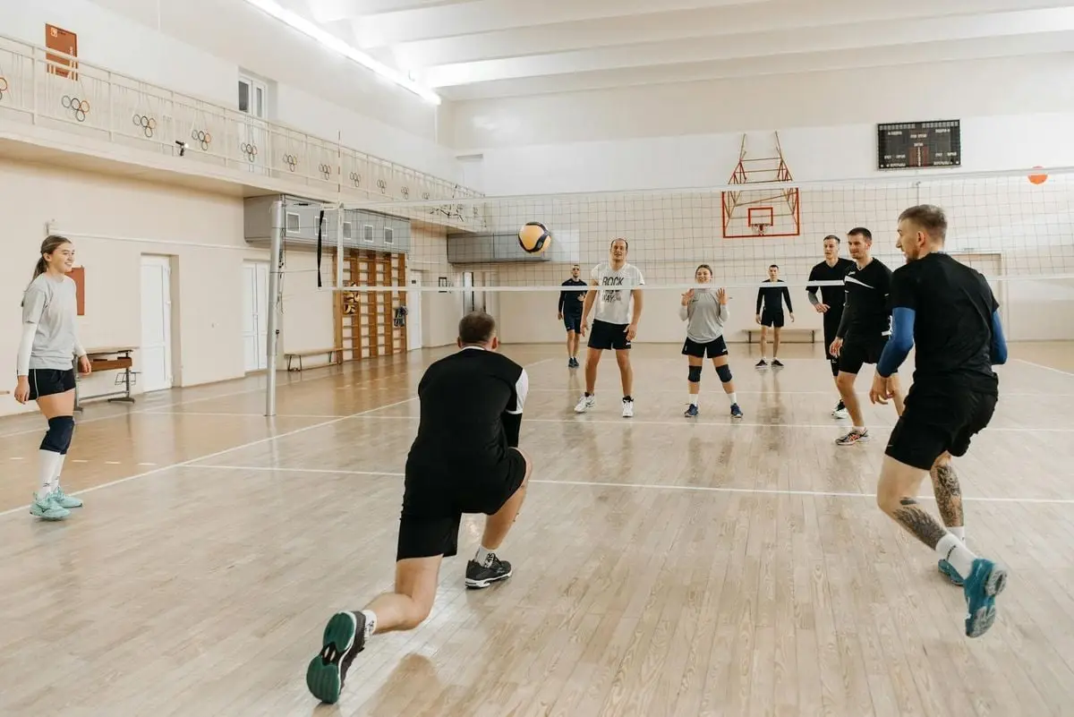 Eight adults play an energetic volleyball game, showcasing teamwork and athleticism on an indoor court.