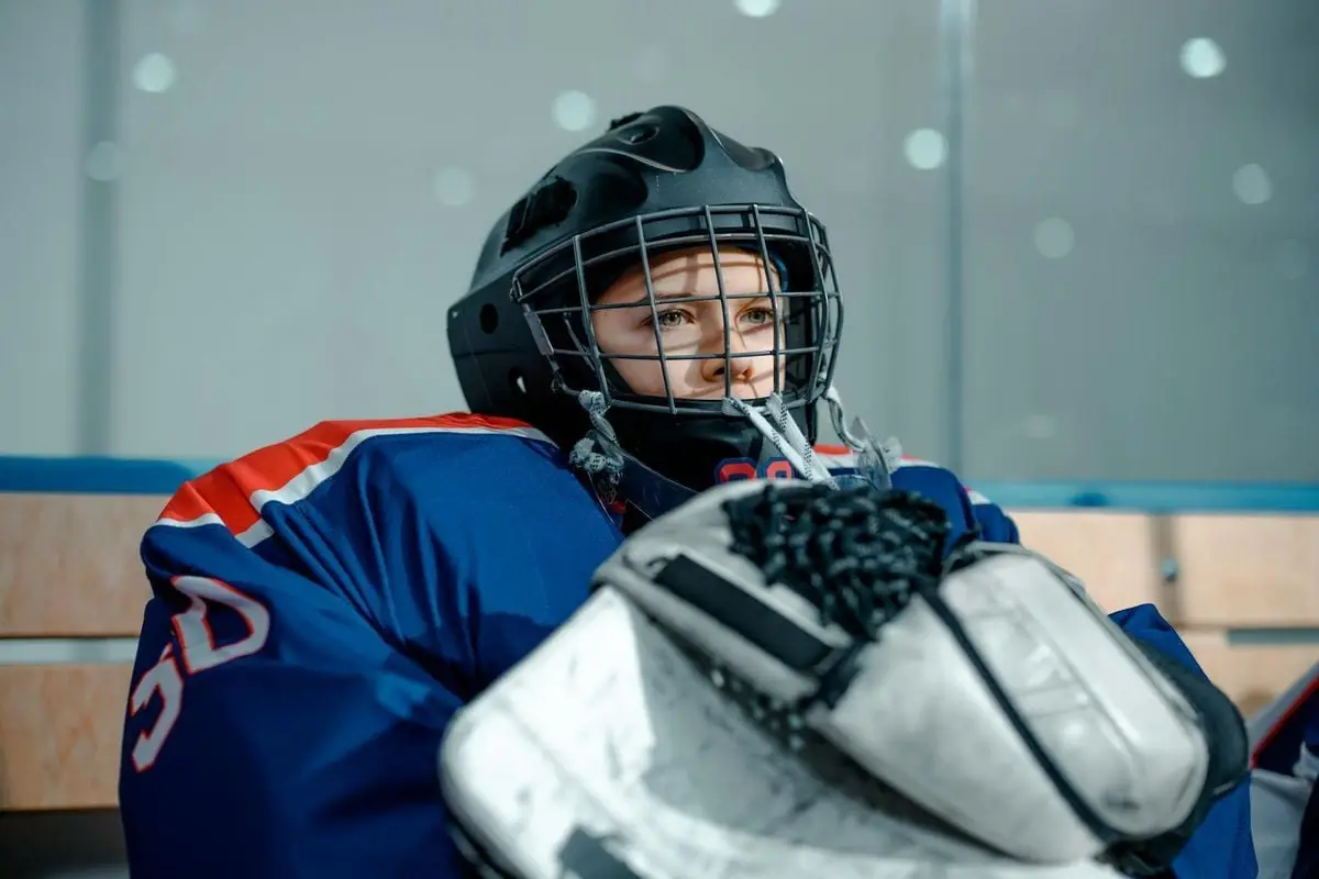 Ice hockey goalie in gear sitting on the bench indoors, concentrating before a game.