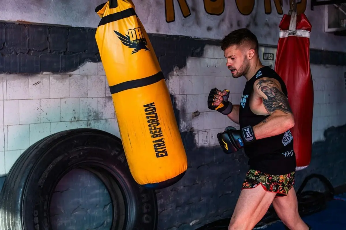 A man practicing boxing techniques with a yellow punching bag indoors.