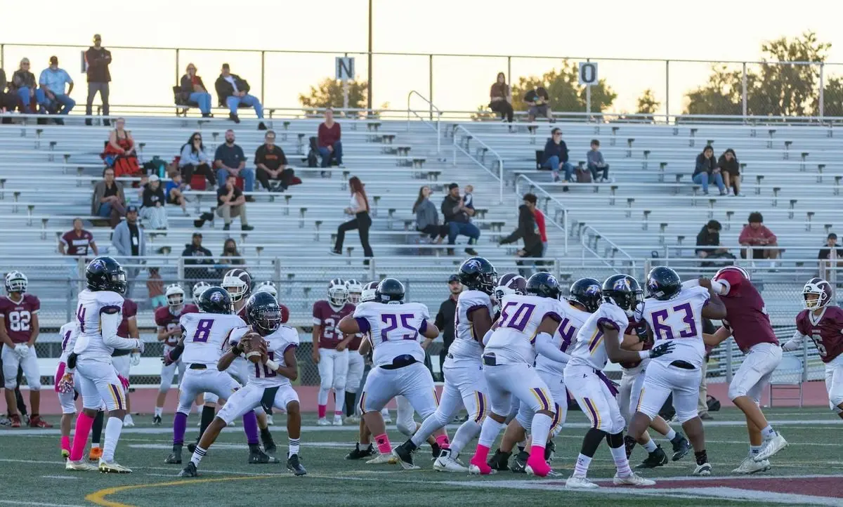 Players compete in a high school American football game with fans in the bleachers.
