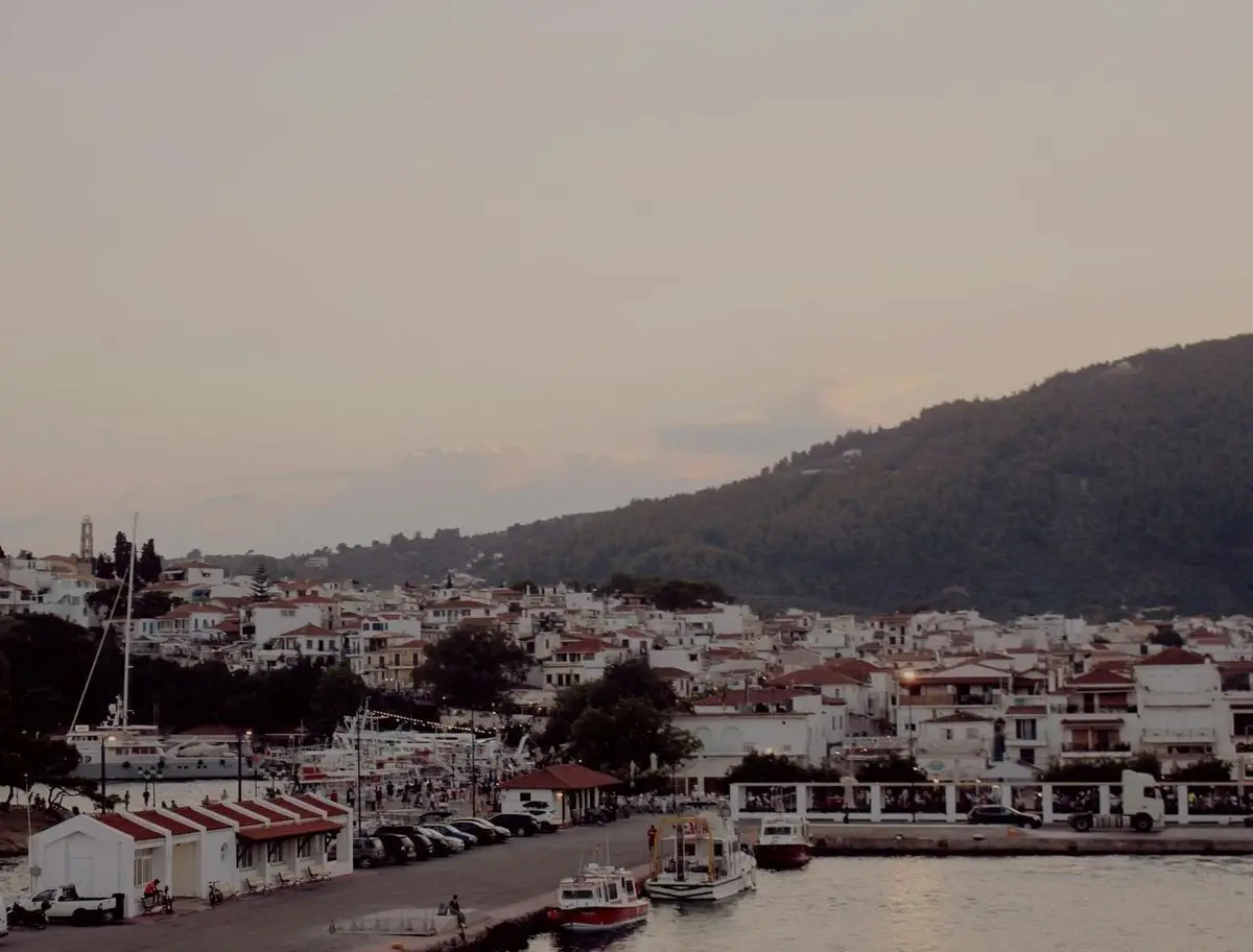 Coastal townscape at sunset featuring moored boats and hillside backdrop.