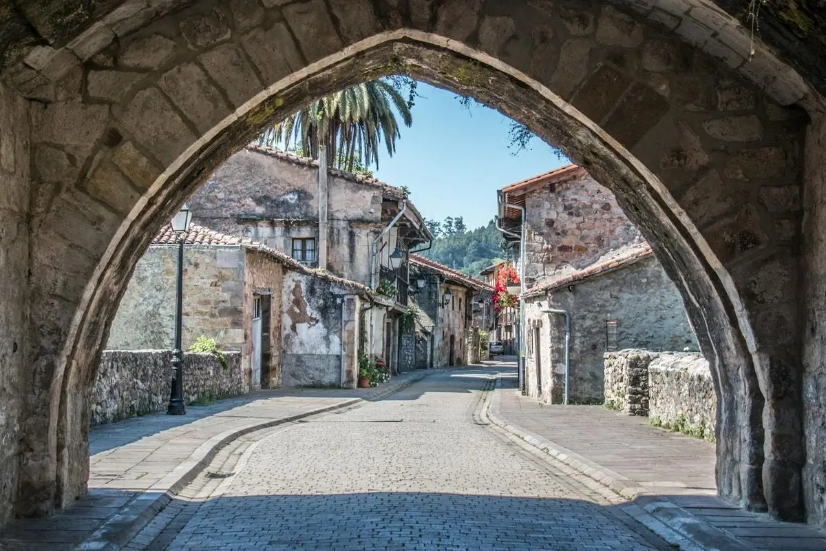 Idyllic cobblestone street view through archway in historic European town with rustic stone buildings.