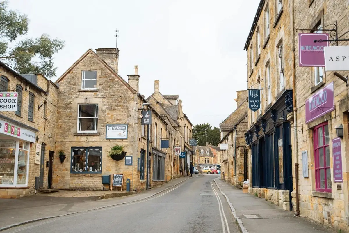 Picturesque village street in the Cotswolds, England featuring historic stone buildings and quaint shops.