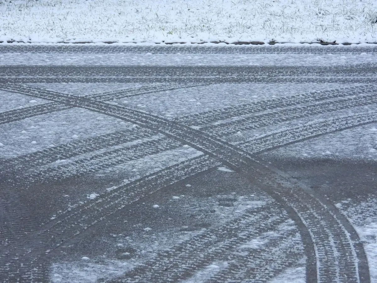 Snow-covered road with intersecting tire tracks and a dusting of snow, illustrating winter conditions.
