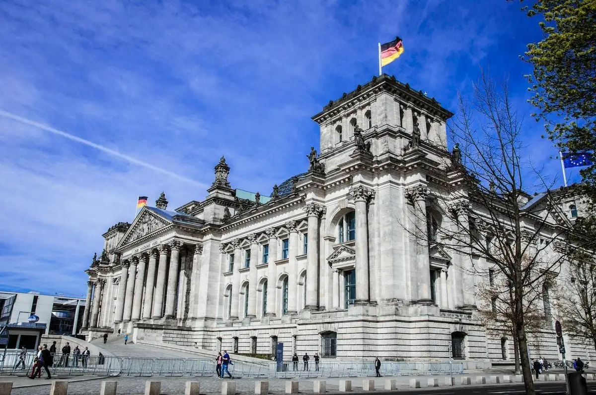 Reichstag building in Berlin with flags under a bright blue sky, showcasing government architecture.