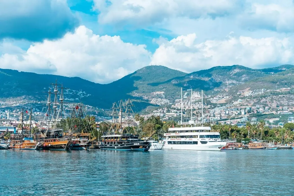 Beautiful Alanya harbor with ships against a backdrop of mountains and vibrant blue sky.