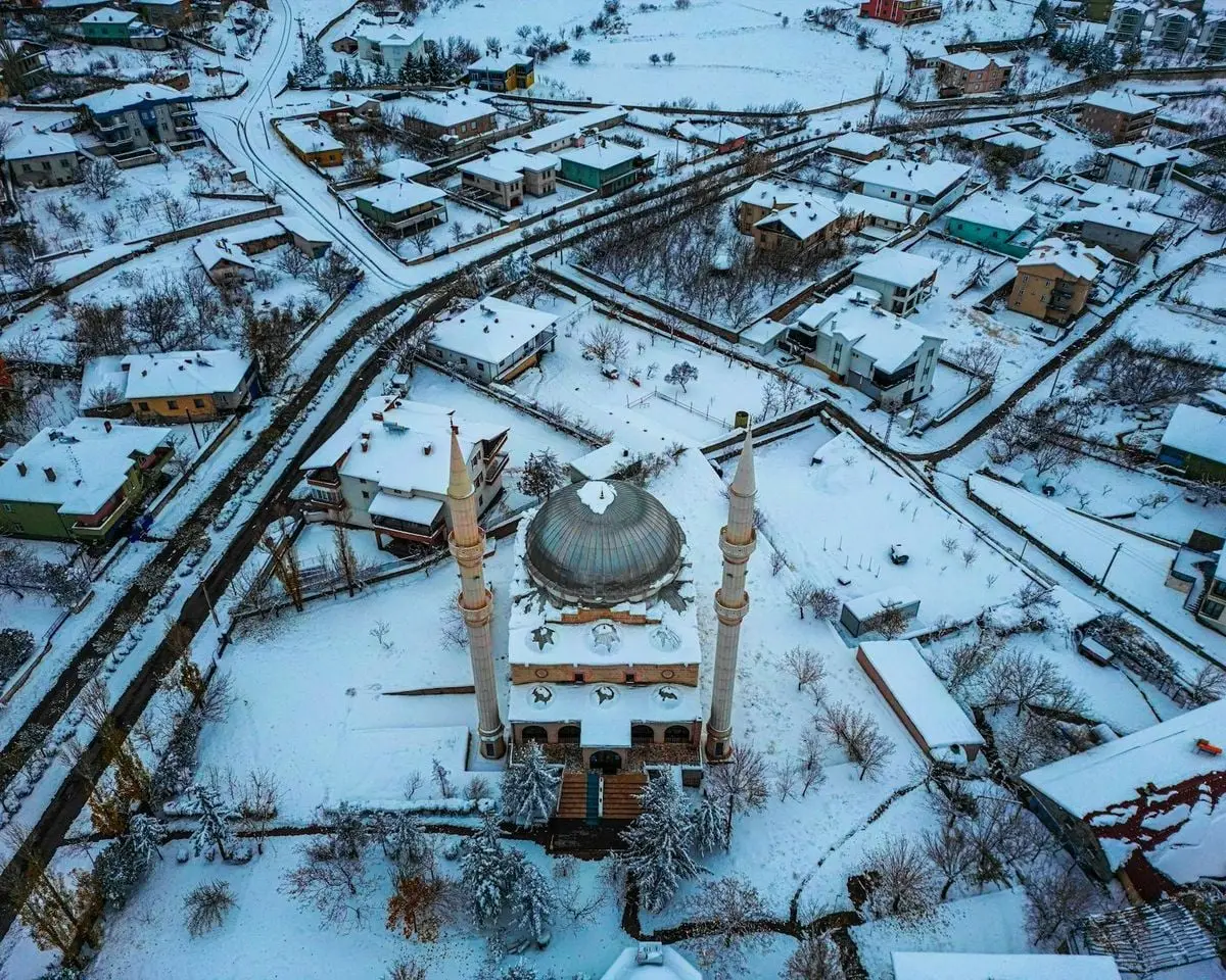 Aerial view of a mosque nestled in a snowy winter village, showcasing an idyllic and serene landscape.