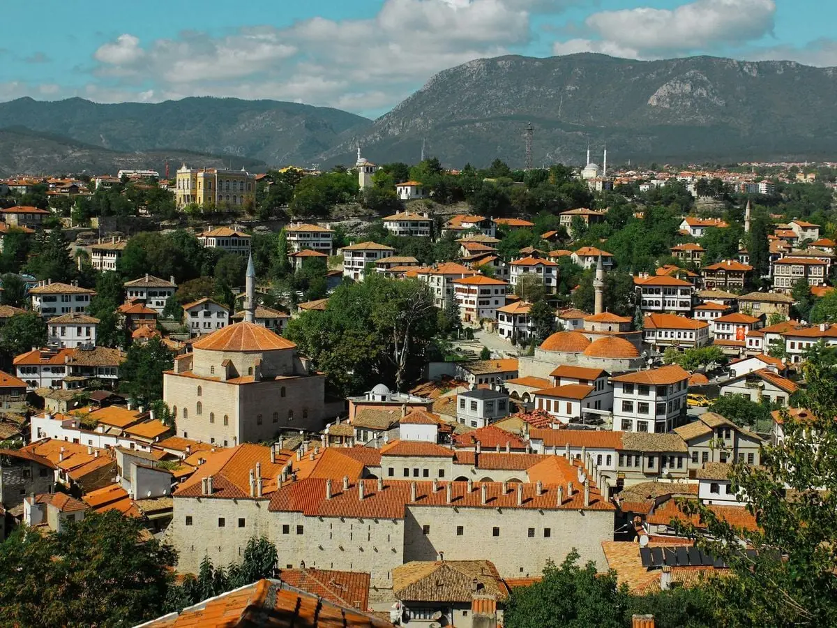 A picturesque view of a historic Turkish town with orange roofs and mountains in the background.