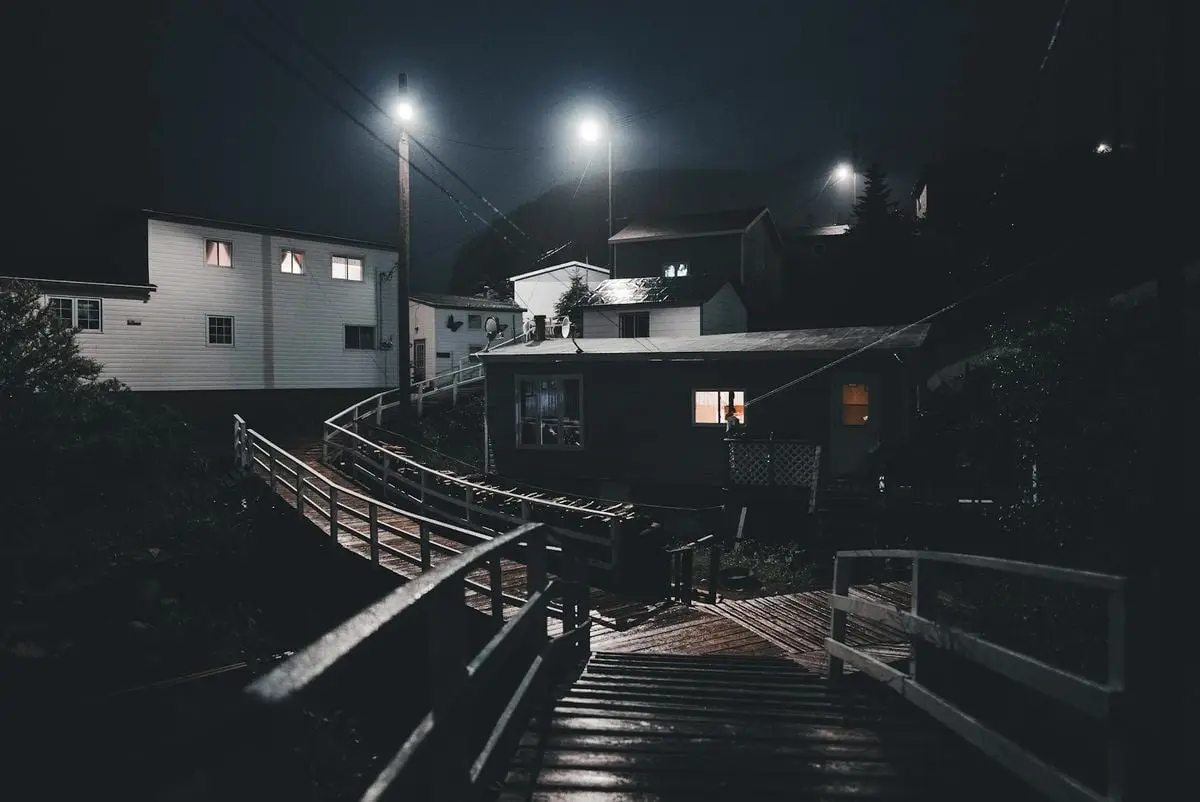 Moody nighttime scene of a quiet wooden neighborhood, illuminated by streetlights.