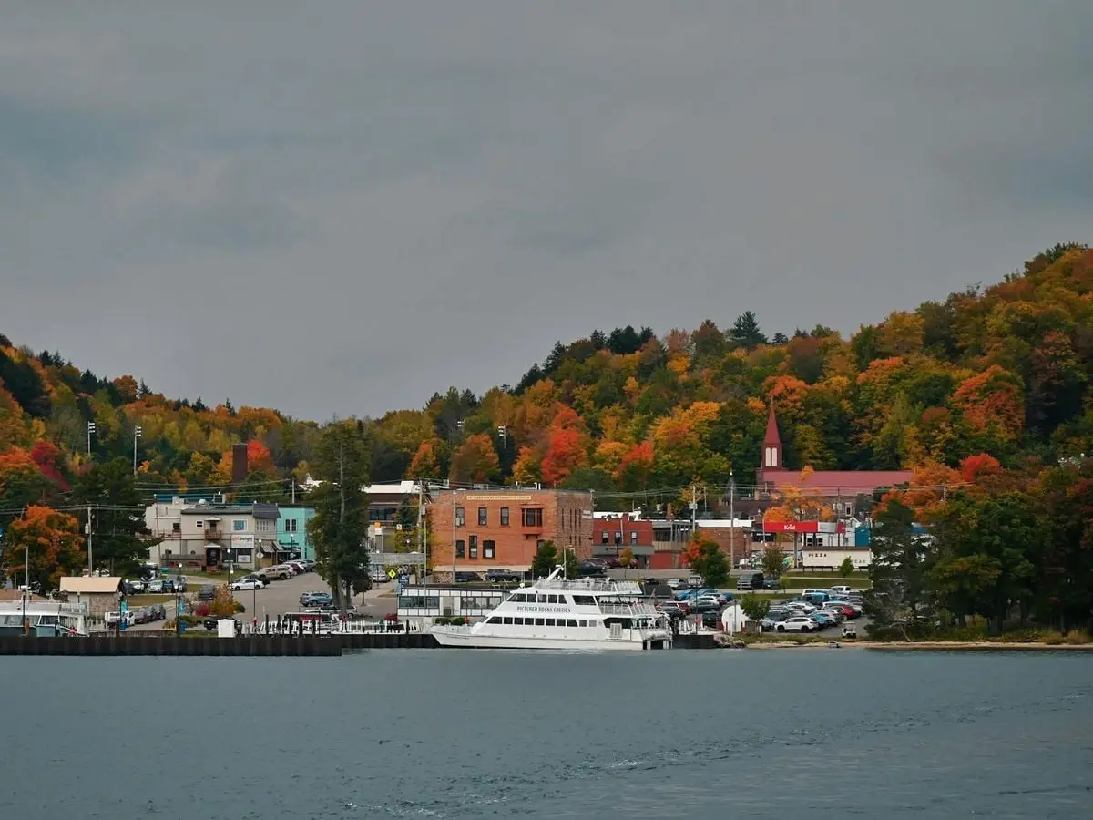 Scenic view of a small lakeside town with autumn foliage and a ferry docked by the shore.