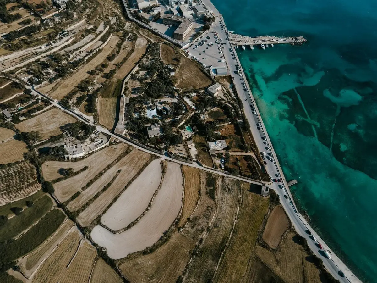 Stunning aerial perspective of Marsaxlokk's coastal area and fields, featuring clear blue waters.