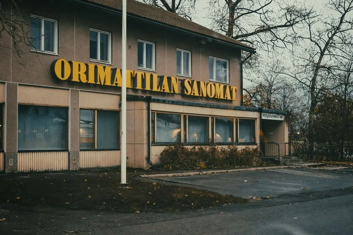 Old Orimattila newspaper building facade with autumn leaves and yellow signage, Finland.