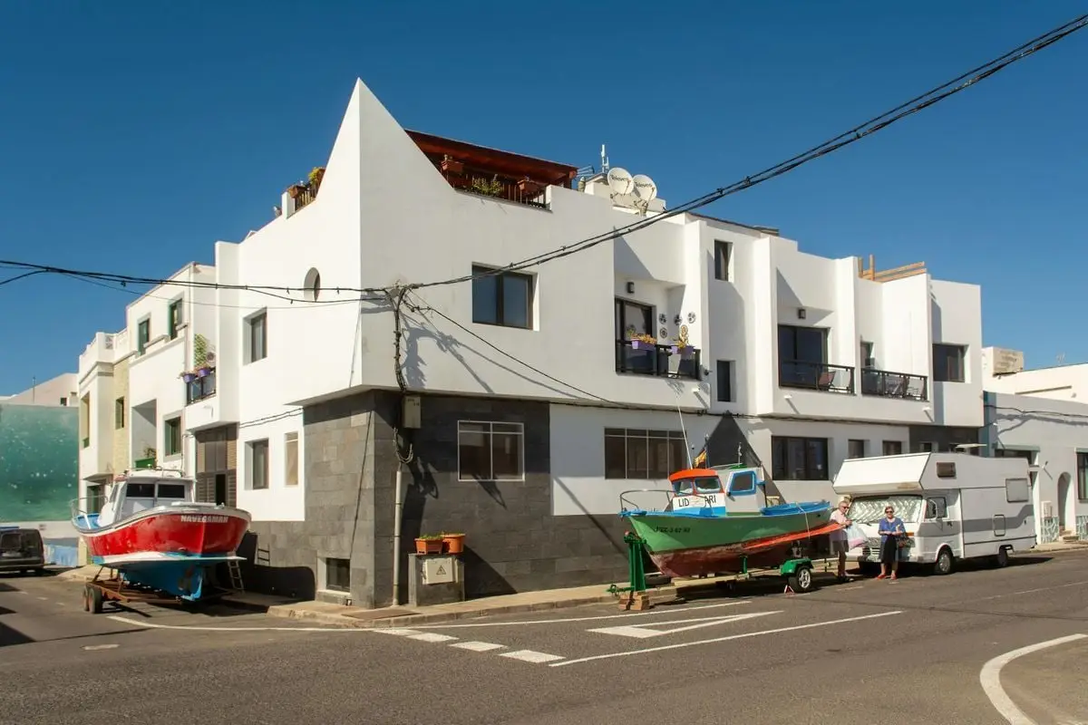 Street scene with boats and a modern building in El Cotillo, Spain, under a clear sky.