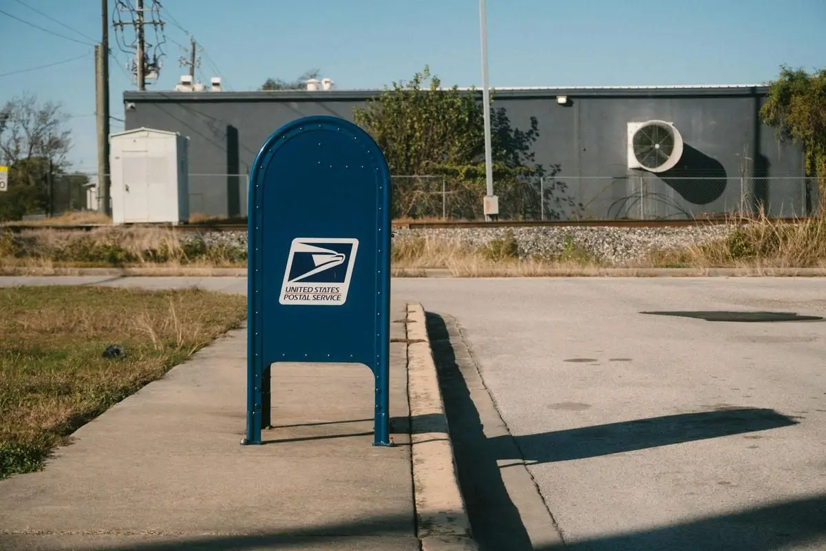 Blue USPS mailbox on a sunny day in a suburban street scene.