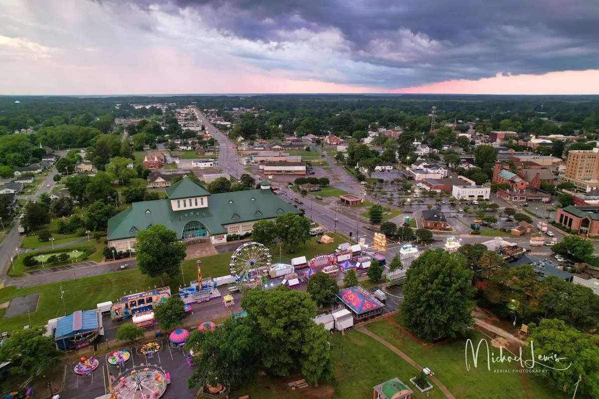 Aerial view showcasing a vibrant town fair with rides and stalls during dusk, under dramatic skies.