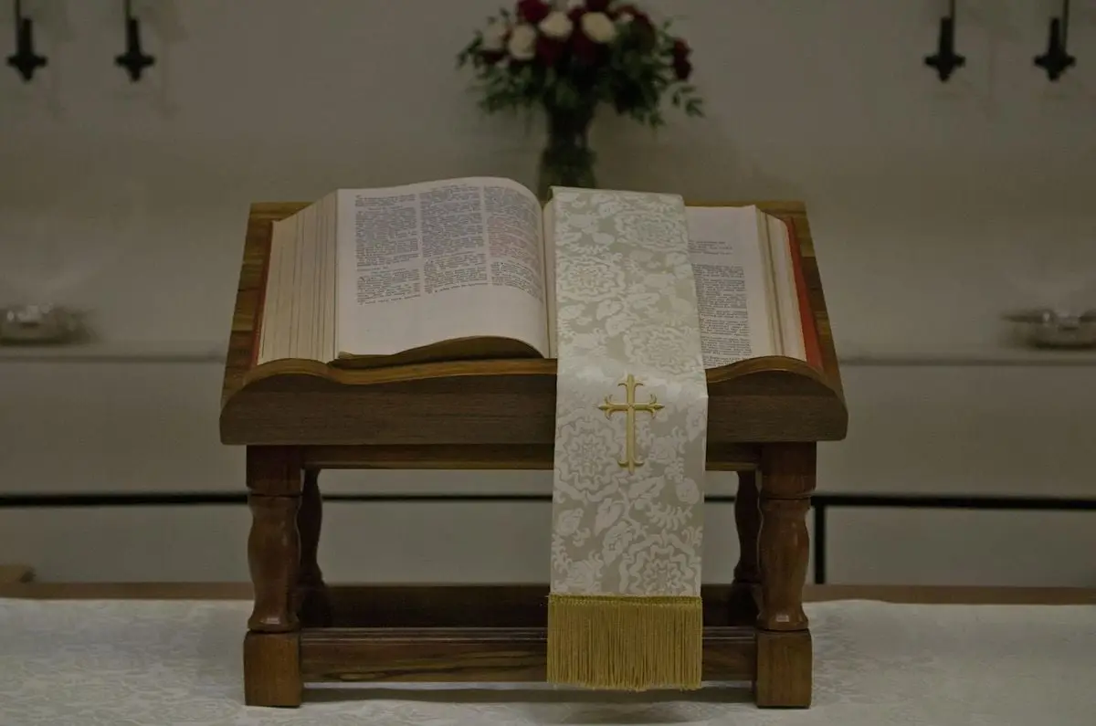 A close-up of an open Bible on a church altar with a cross-embroidered cloth in a religious setting.