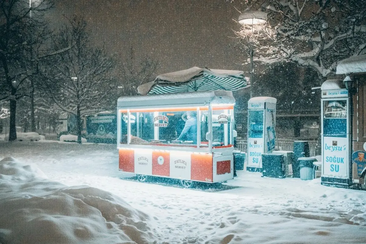 A delightful sweet vendor cart offers warmth and snacks in a snowy Konya night.