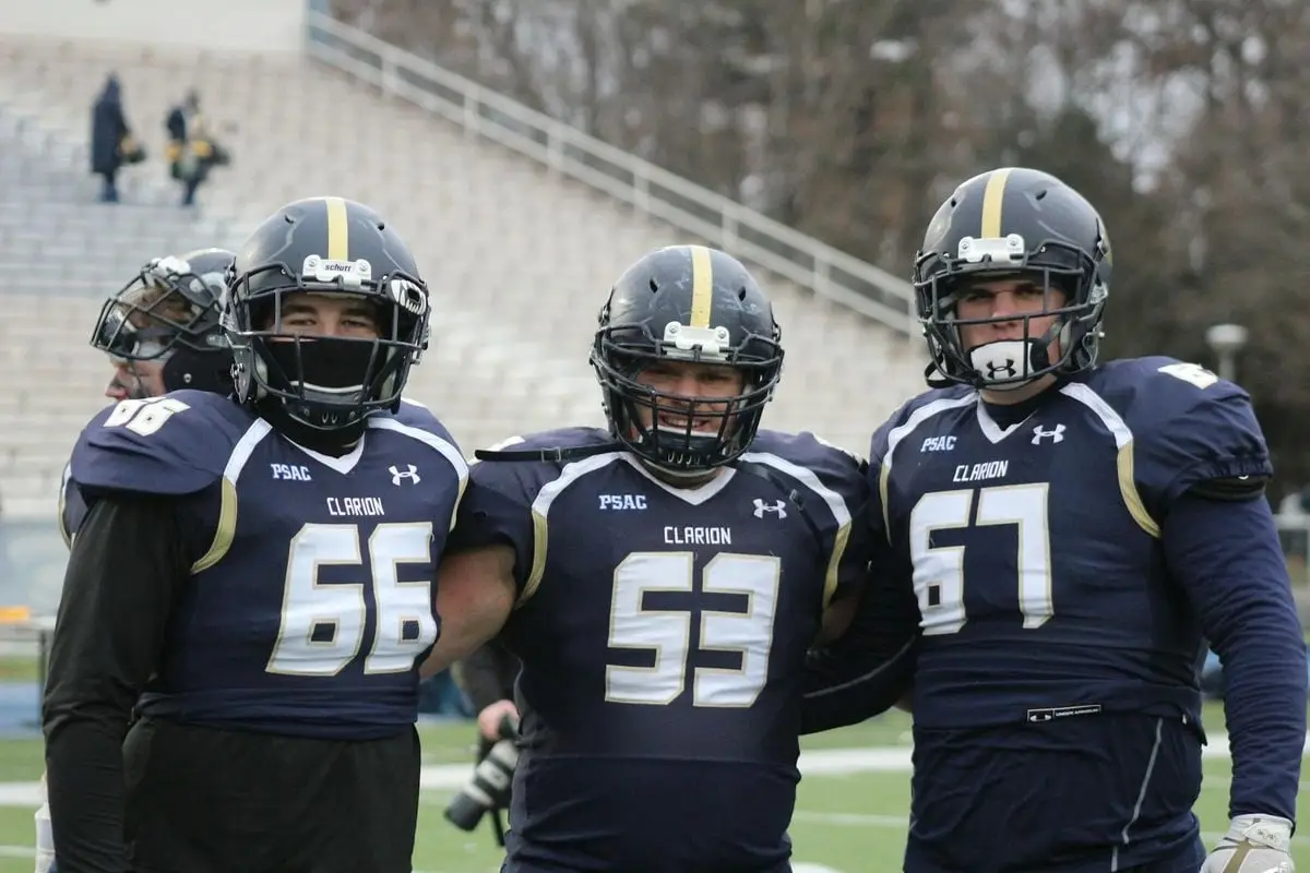 Three football players pose in uniforms at a college stadium, showcasing teamwork and sportsmanship.