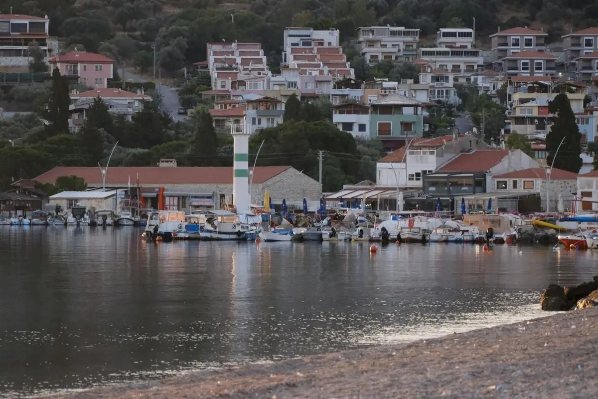 Serene harbor scene in Foça, İzmir with boats and hillside houses at dusk.