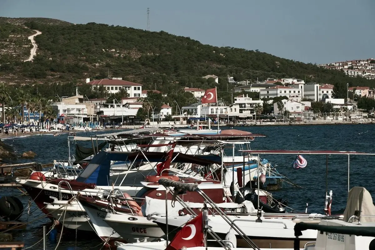 Charming view of Foça's coastal harbor featuring moored boats and scenic townscape under a clear sky.
