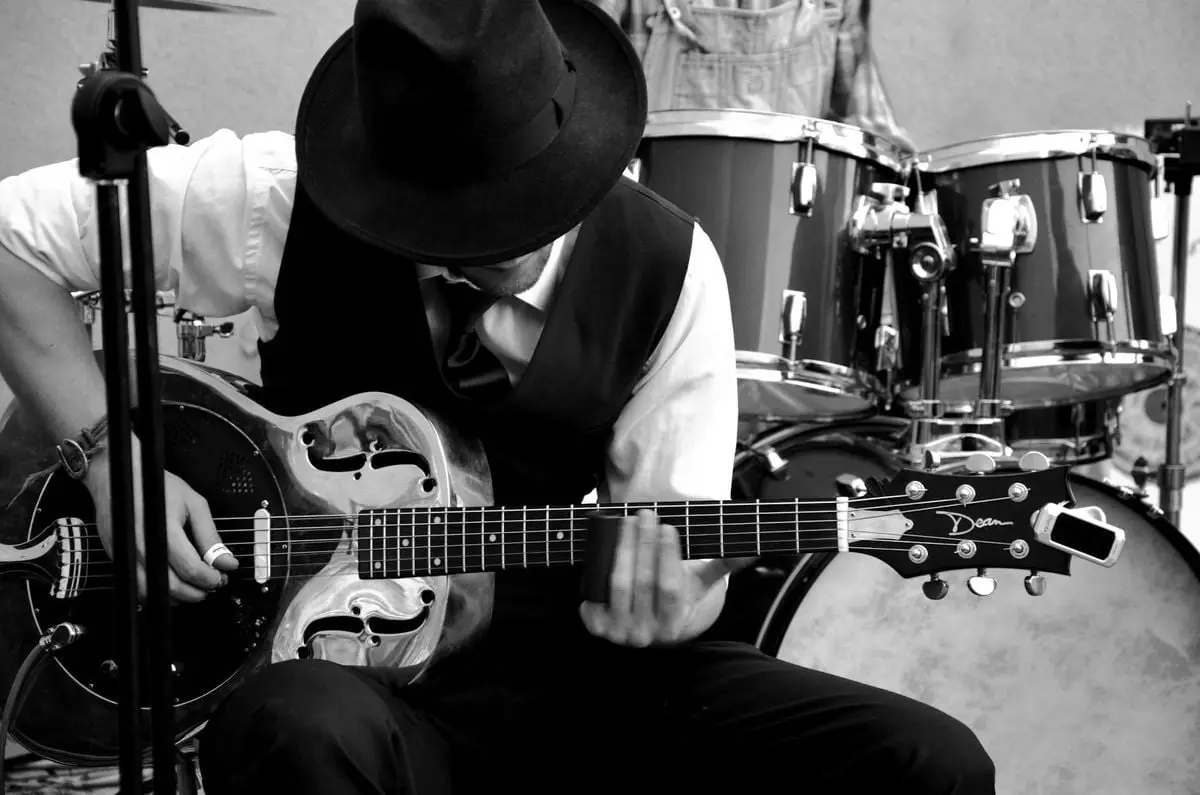 Musician playing guitar with a drum set in a black and white setting.