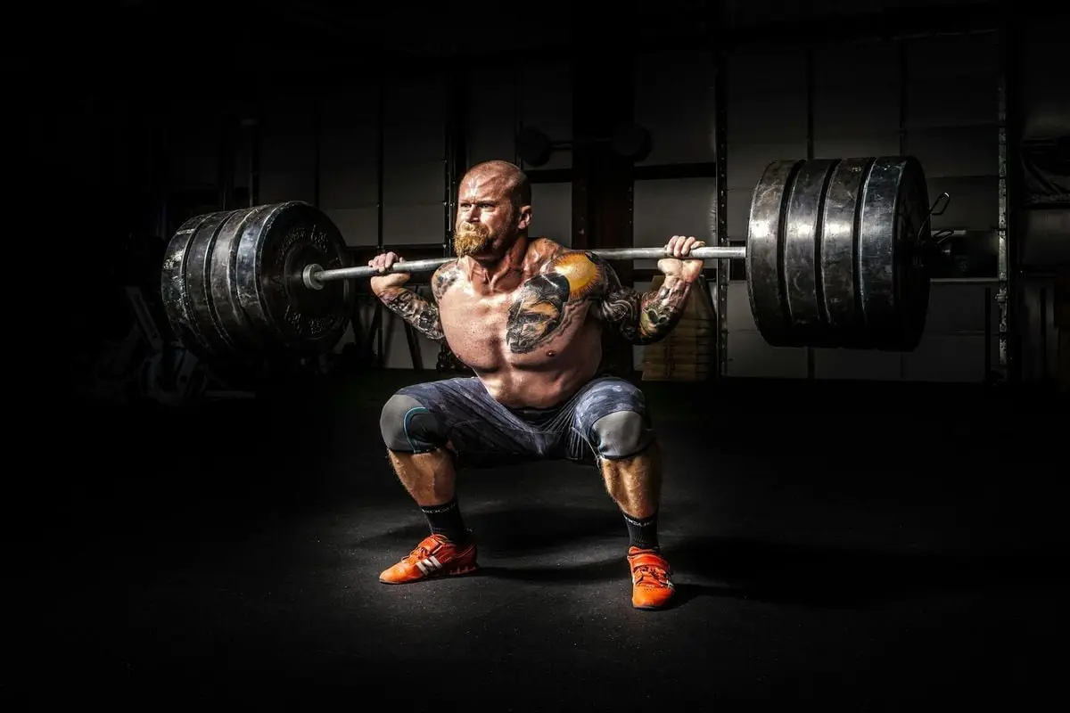 Muscular man lifting heavy weights during an intense squat session inside a gym.