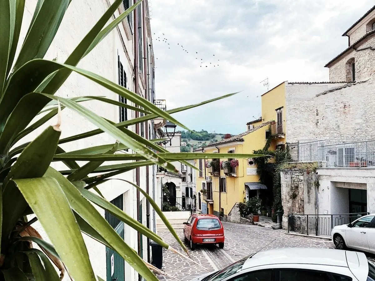 Quaint cobblestone street in Manoppello, Italy with colorful buildings and parked cars.