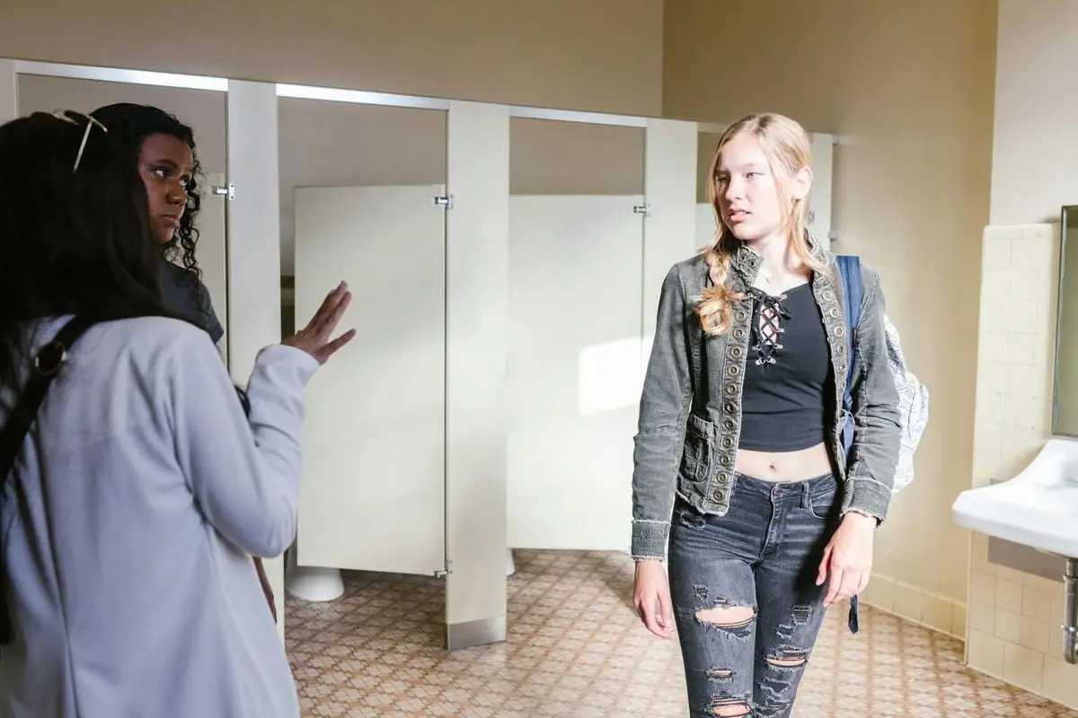 Teen girls interact in a school bathroom, focusing on communication and social dynamics.