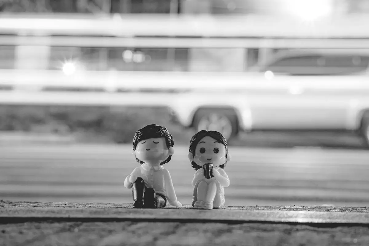 Charming couple figurines sitting on roadside in black and white with blurred motion background.