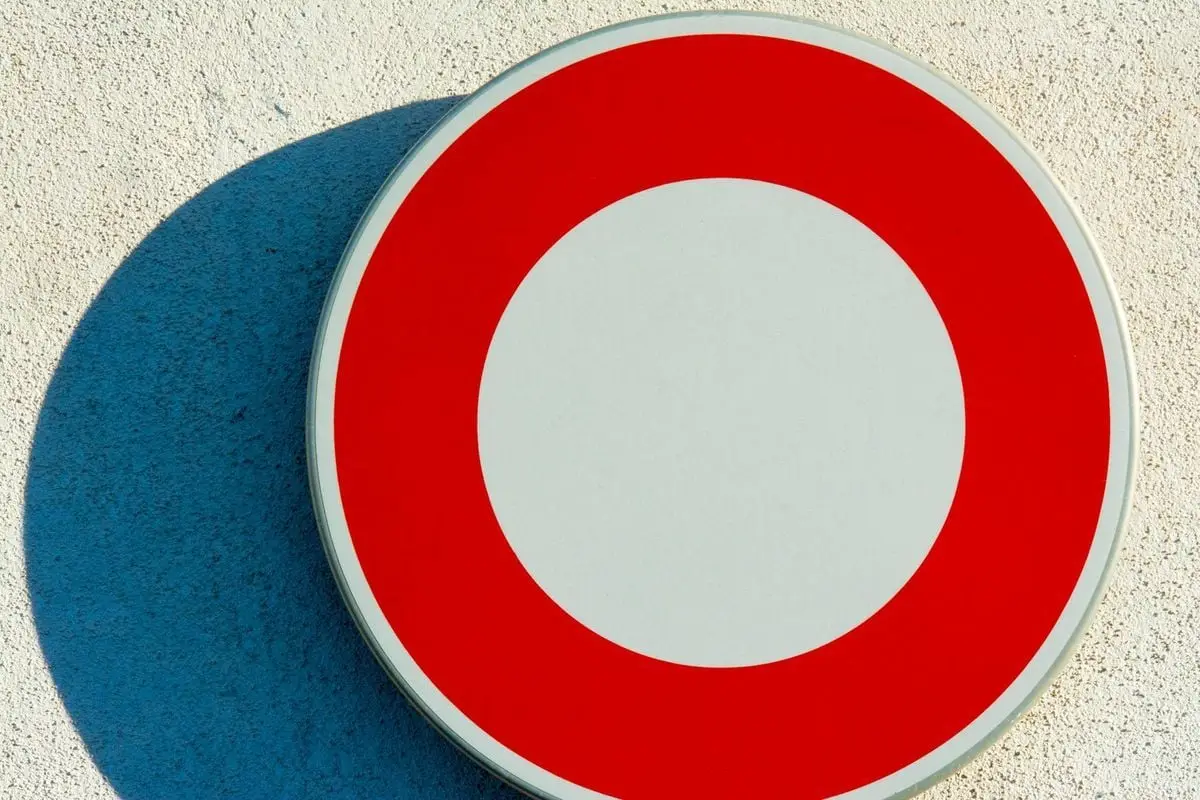 A clear red and white prohibition sign attached to a textured wall in daylight.
