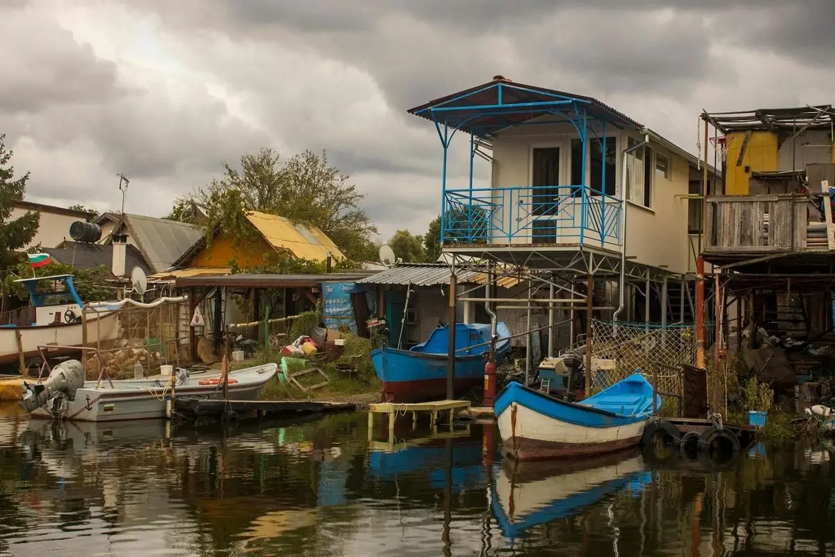 Charming rural Bulgarian village with boats docked along the river, showcasing rustic architecture.