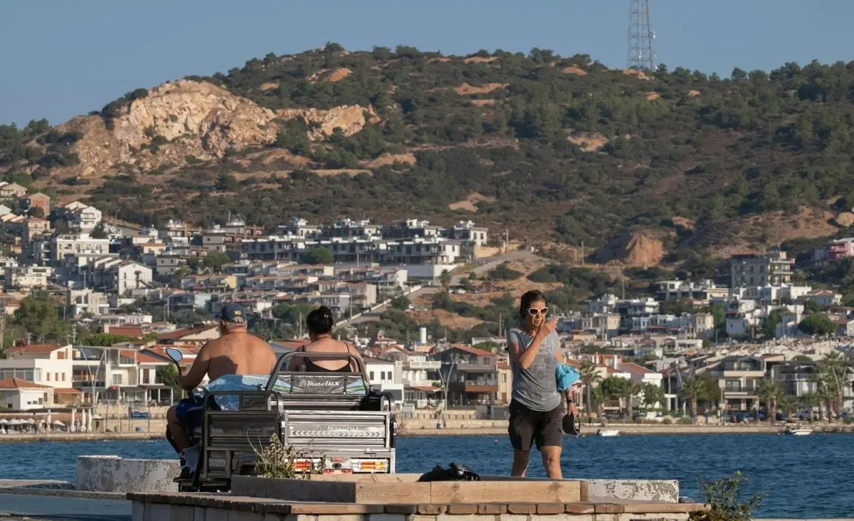 Lively coastal scene in Foça, İzmir with people and stunning hillside backdrop.