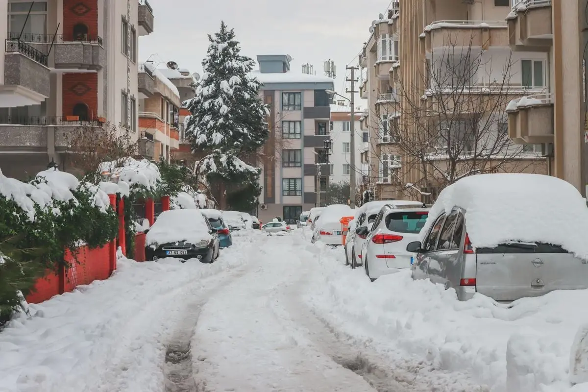 A residential street in Gaziantep, Turkey, blanketed in snow with parked cars and buildings.