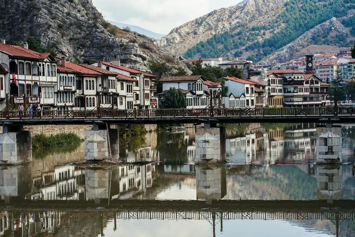 Picturesque riverfront houses and bridge in Amasya, Turkey with mountain backdrop.