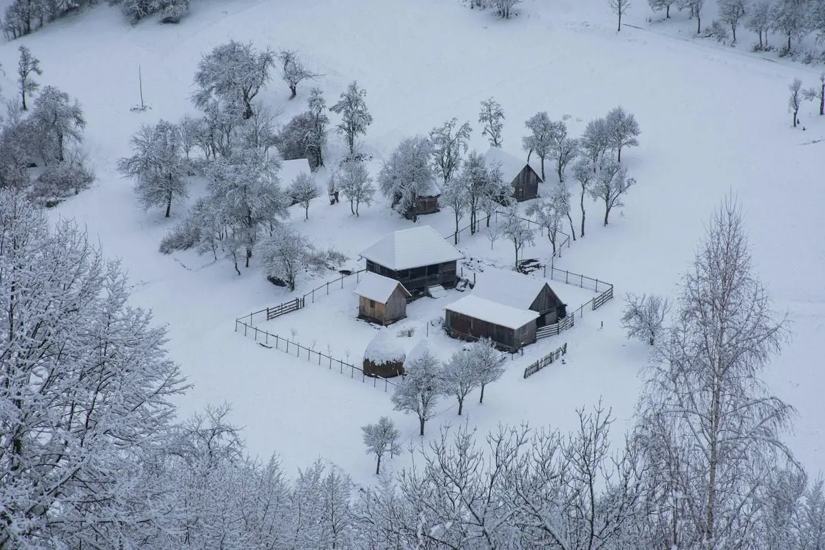 A serene aerial view of a snow-covered village in Sartăș, Romania, during winter.