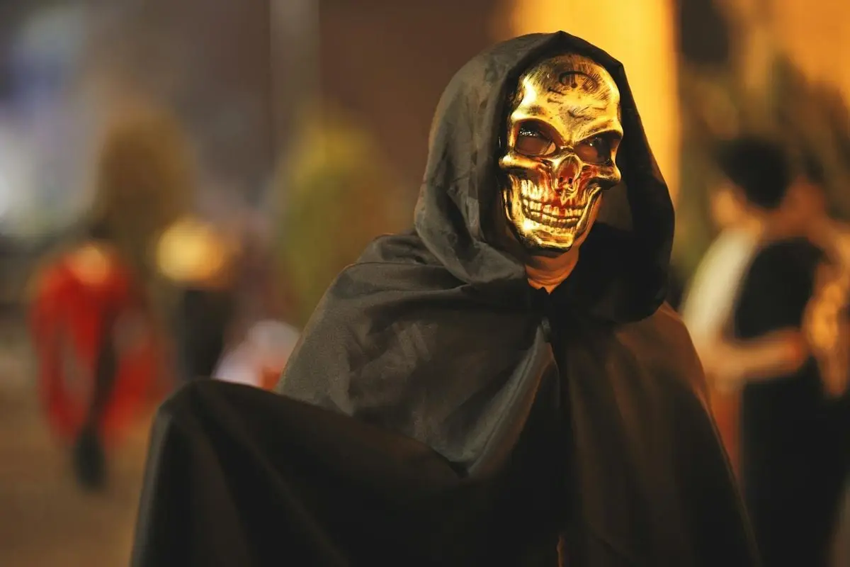 A person in a golden skull mask and black cloak at a night parade in Arequipa, Peru.