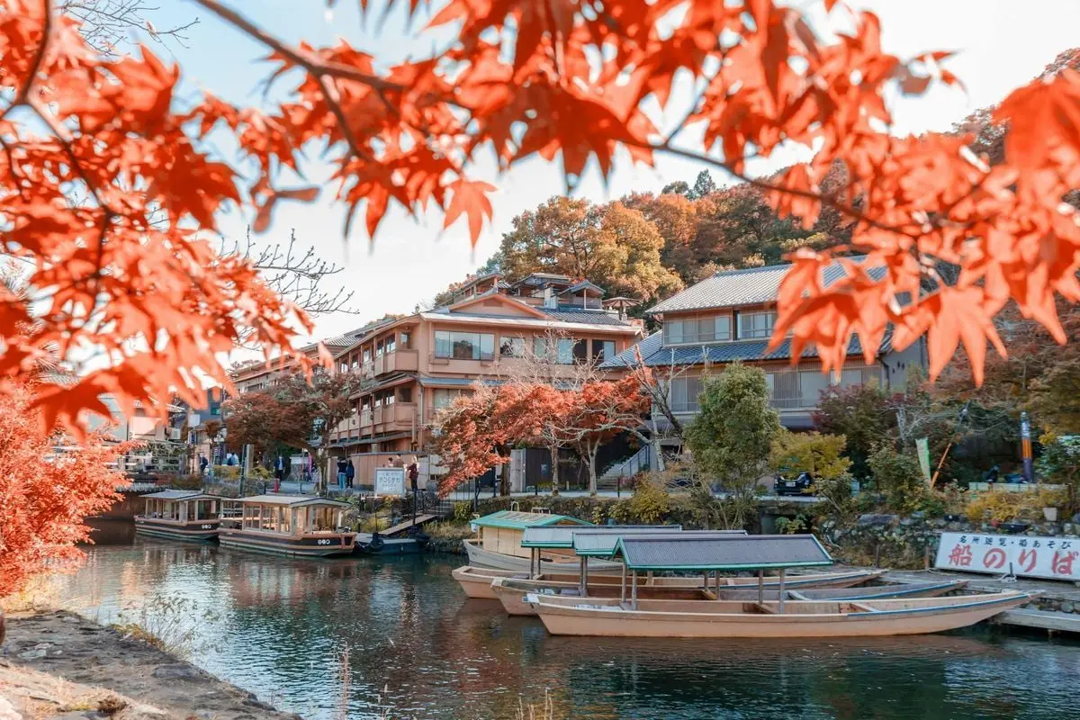 A picturesque scene with wooden boats docked by a river lined with vibrant red autumn leaves in Japan.