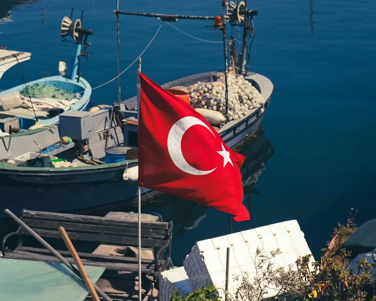 Turkish flag waving near fishing boats in a sunny marina, capturing a vibrant coastal scene.