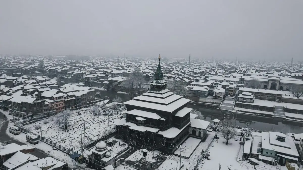 Aerial view of snow-covered Srinagar city, showcasing a traditional mosque in winter scenery.