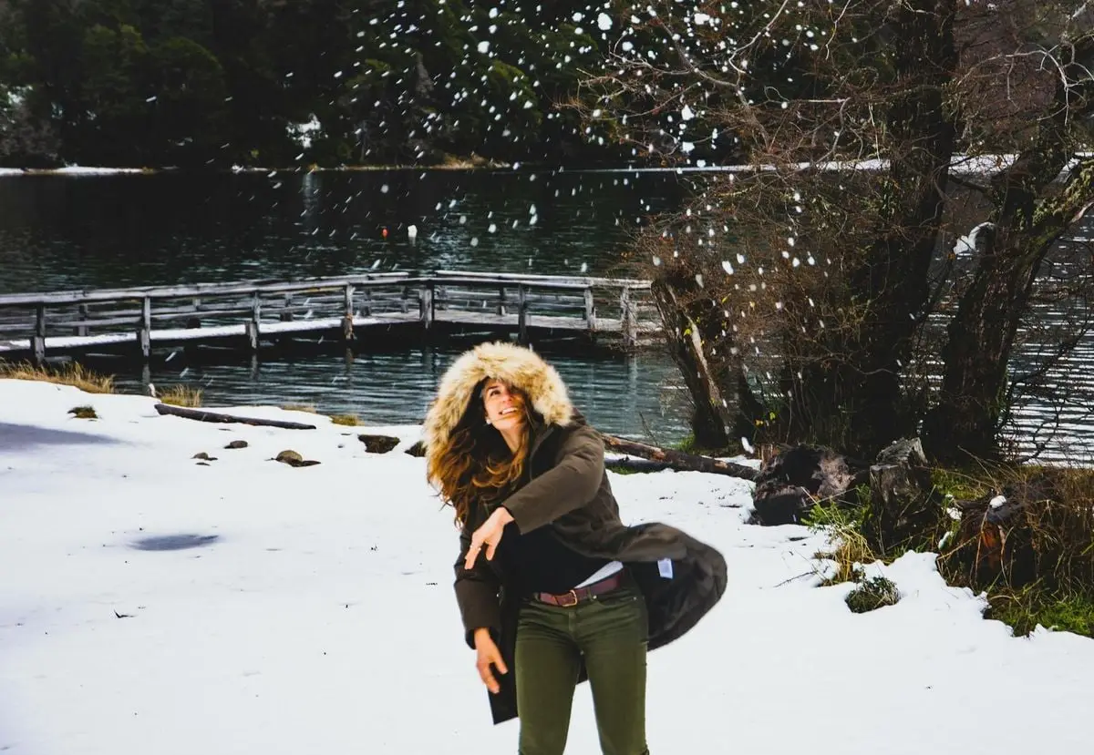 Woman enjoying winter day, playing with snow by a scenic lake in San Martin de los Andes, Argentina.