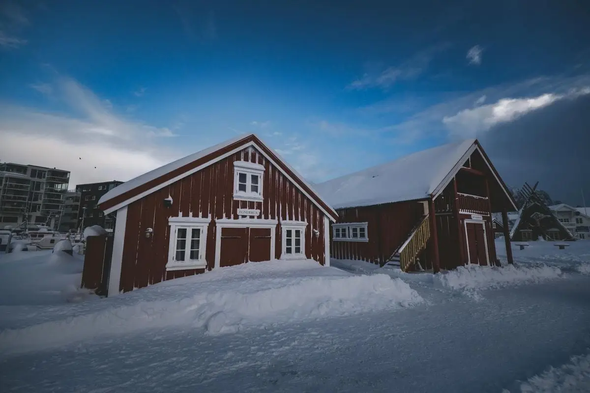 Picturesque red wooden buildings covered in snow in a serene winter village setting.