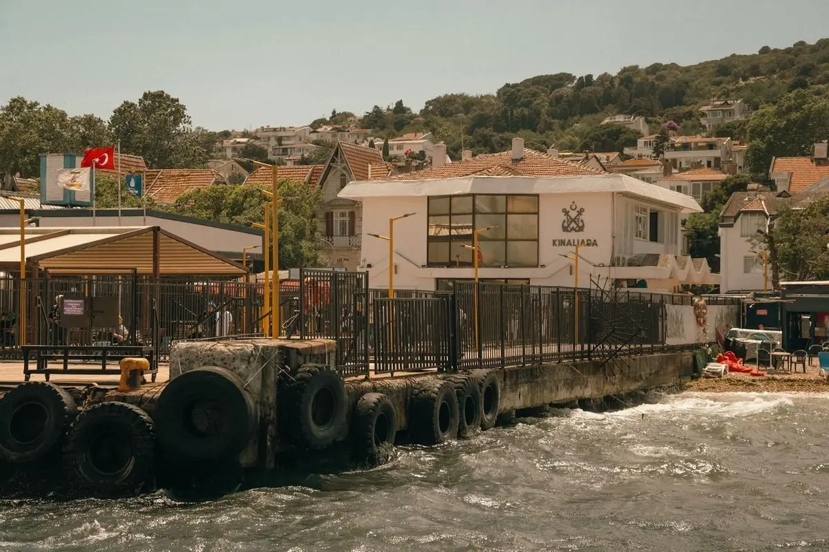 Scenic view of Kınalıada ferry station surrounded by water and buildings under a sunny sky.