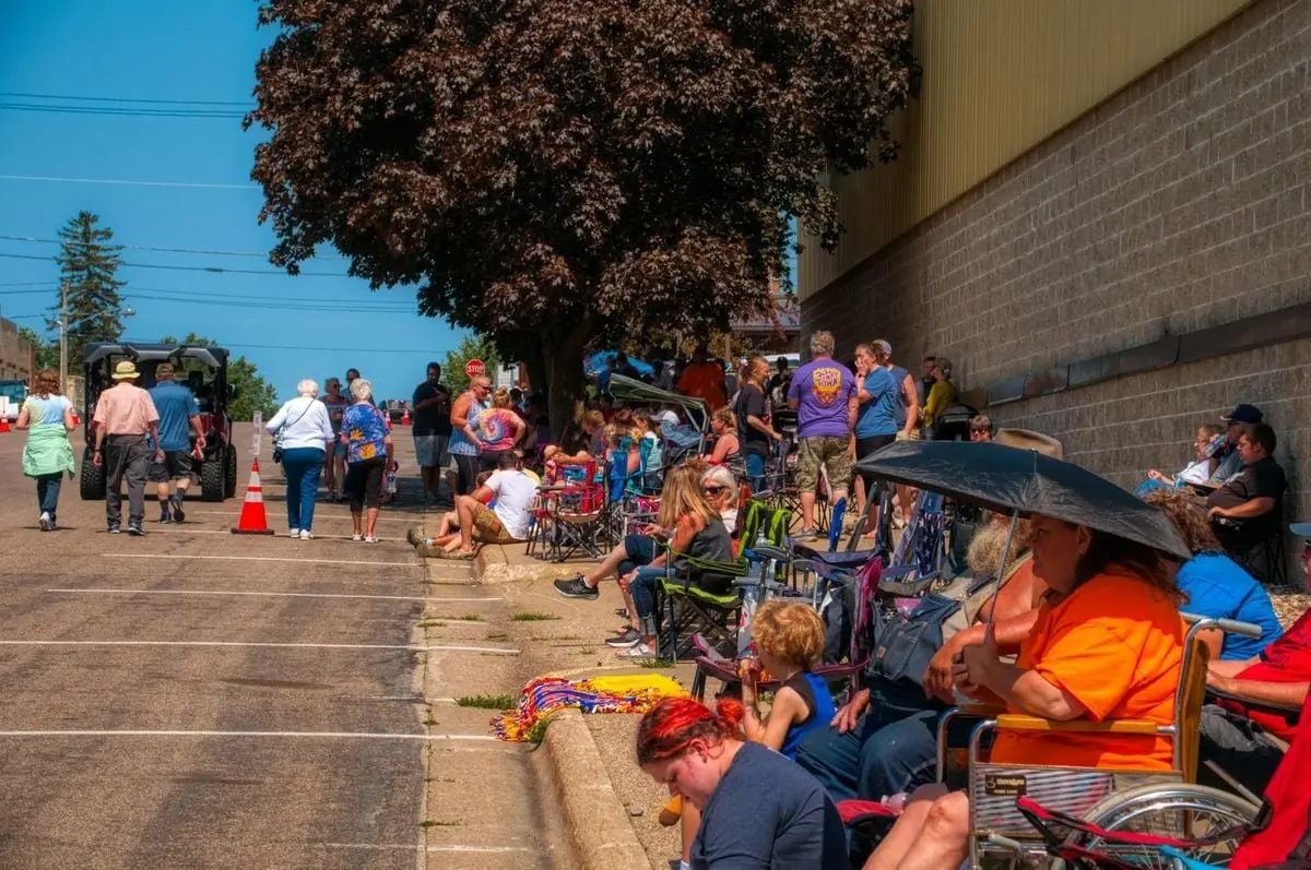 A vibrant scene of people gathering on a sunny street in Plainview, MN, during a summer event.